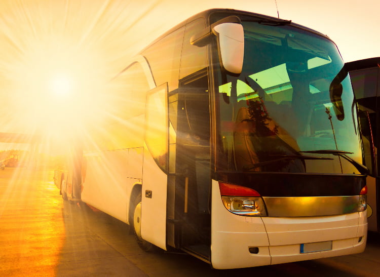 A charter bus parks with the setting sun behind it